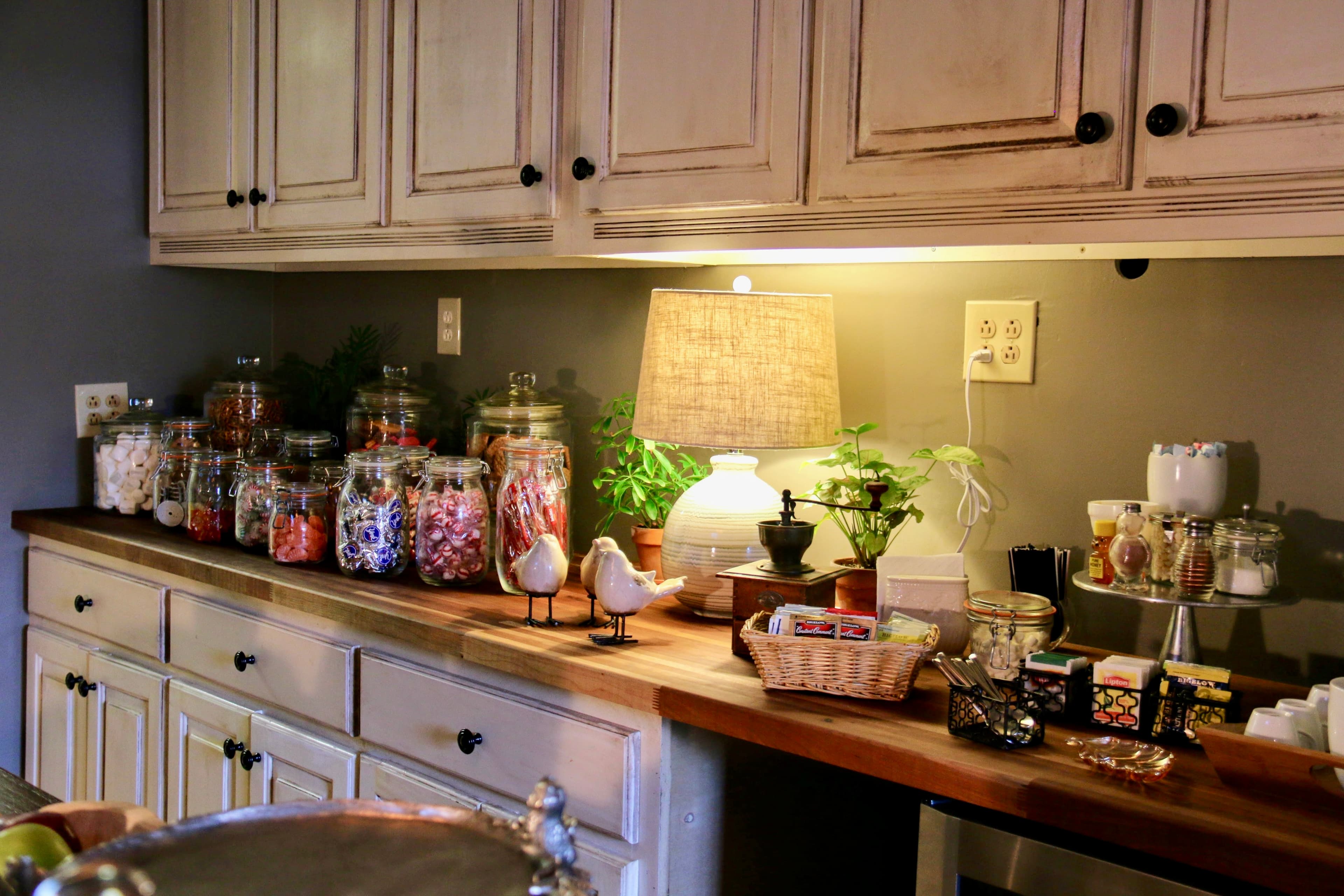 A well-organized kitchen countertop featuring jars of candy, plants, a lamp, and assorted kitchen items.