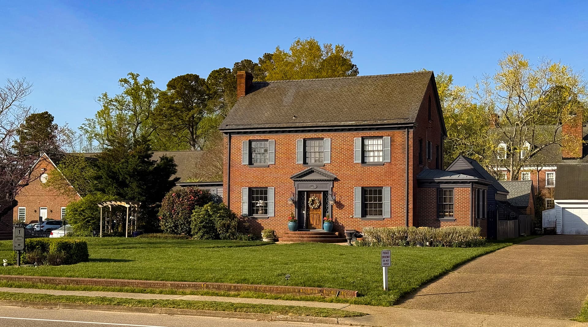 Red brick house with a grassy yard and blue sky in the background.